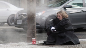 A woman tries to keep warm on a grate on a street corner in downtown Toronto on Monday, Jan. 5, 2014. (Colin Perkel / THE CANADIAN PRESS)