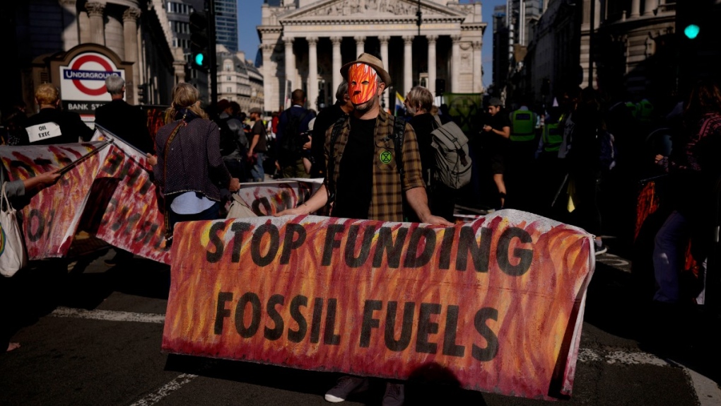 An Extinction Rebellion climate change activist holds a banner backdropped by the Bank of England, at left, and the Royal Exchange, centre, in the City of London financial district, on Sept. 2, 2021. (Matt Dunham / AP) 