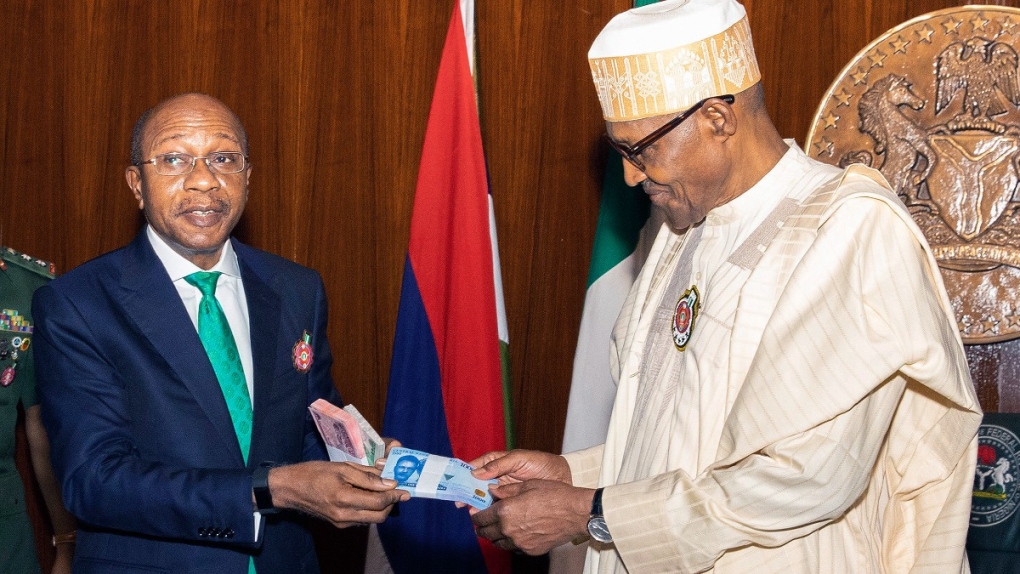 In this photo released by the Nigeria State House, Nigeria's central bank governor, Godwin Emefile, left, presents the newly designed currency notes to Nigeria's President Muhammadu Buhari, right, during a launch in Abuja, Nigeria, on Nov. 22, 2022. (Sunday Aghaeze / Nigeria State House via AP) 