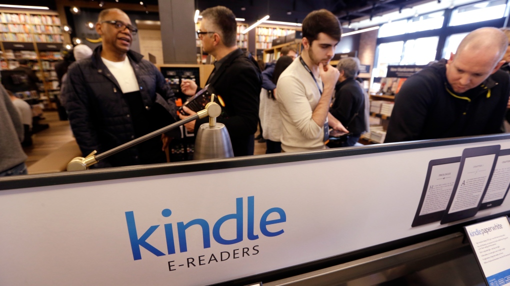 Customers stand near a display of Kindle electronic readers at the opening day for Amazon Books, the first brick-and-mortar retail store for online retail giant Amazon, on Nov. 3, 2015, in Seattle. (AP Photo/Elaine Thompson)