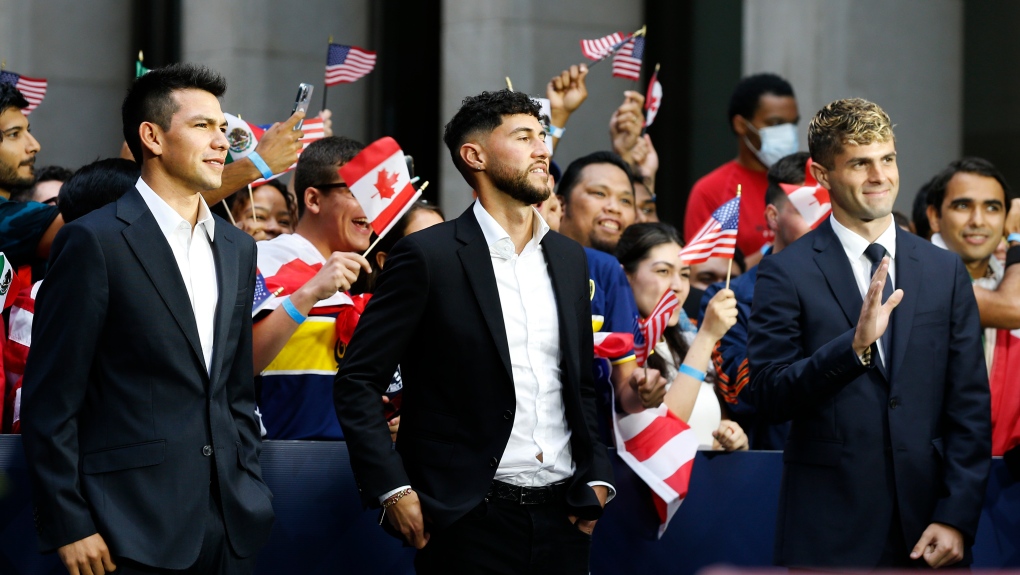 International soccer players, from left, Hirving "Chucky" Lozano, Jonathan Osorio and Christian Pulisic wait along 6th Ave. for FIFA's announcement of the names of the host cities for the 2026 World Cup soccer tournament, Thursday, June 16, 2022, in New York. (AP Photo/Noah K. Murray)