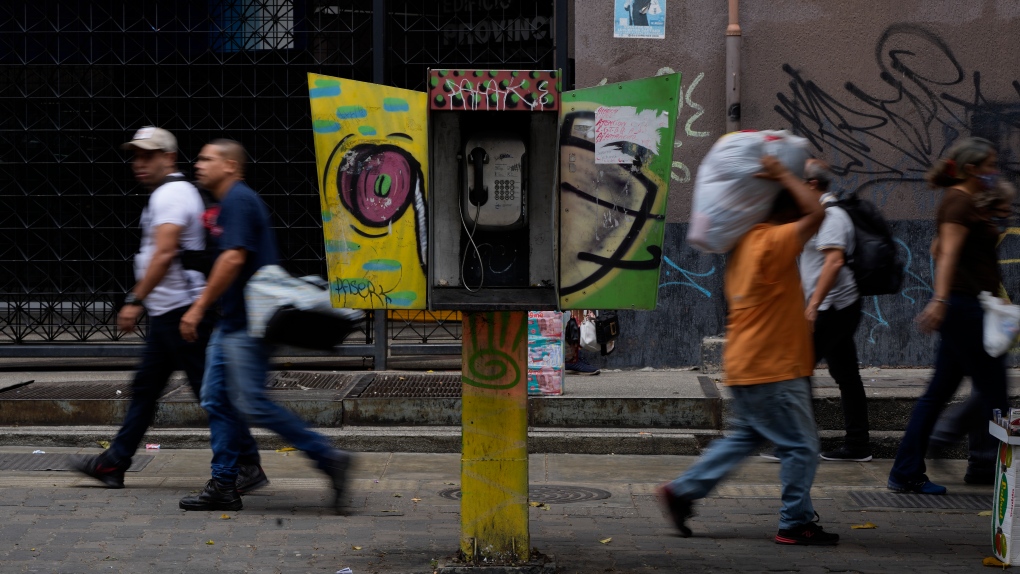 Pedestrians walk past an out of service National Telephone Company of Venezuela, CANTV, phone booth, in Caracas,Venezuela, Friday, May 13, 2022.  (AP Photo/Ariana Cubillos)