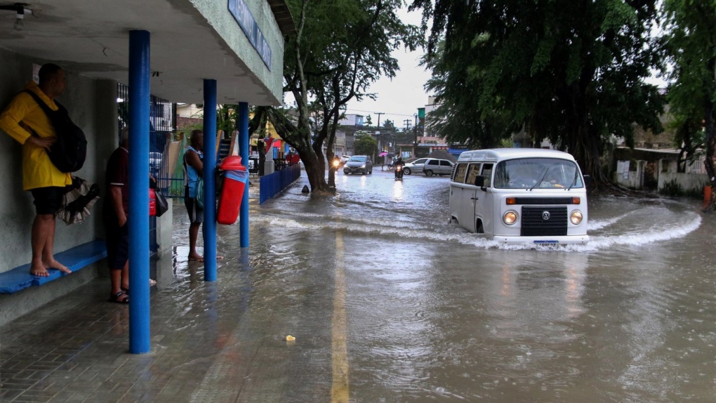 A woman stands on a bus stop bench as a driver of a Volkswagen van navigates a flooded street in Recife, state of Pernambuco, Brazil, May 28, 2022. (AP Photo/Marlon Costa/Futura Press)