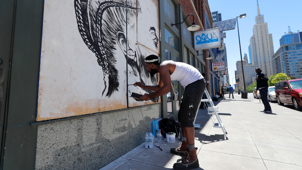 Artist Gabriel Thomas paints a mural of deceased rapper Nipsey Hussle on Guns and Roses boutique storefront in downtown Dallas, Wednesday, June 10, 2020. (AP Photo/Tony Gutierrez)
