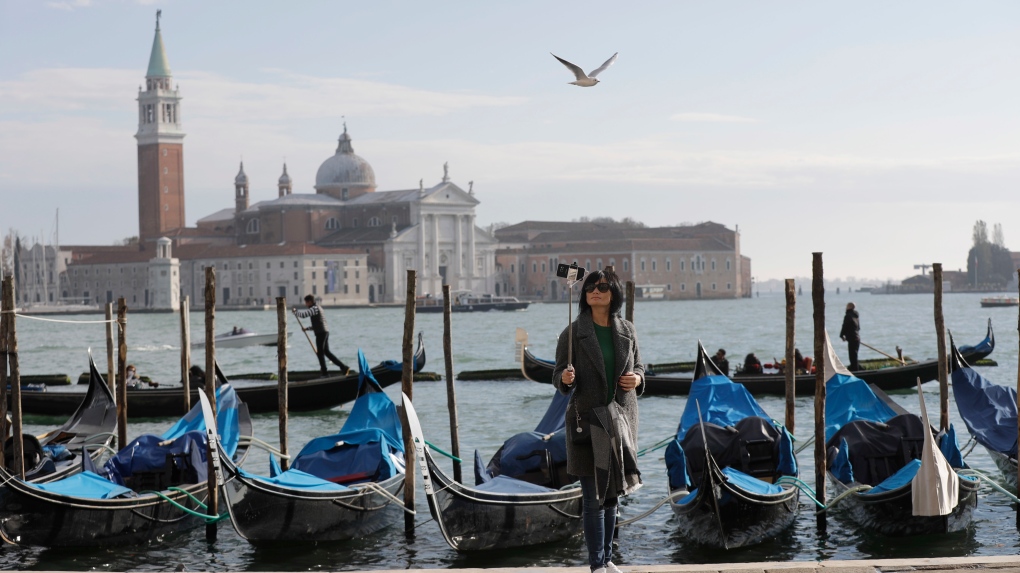 FILE - A tourist takes a selfie in St. Mark's Square in Venice, Italy, Nov. 12, 2016. Starting in January, Venice will oblige day-trippers to make reservations and pay a fee to visit the historic lagoon city. (AP Photo/Luca Bruno, File)