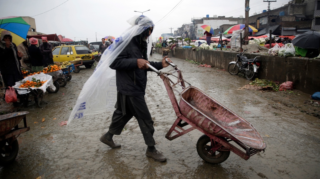 A man covers himself with a plastic sheet to protect from the rain at a market in Islamabad, Pakistan, Jan. 22, 2022. (AP Photo/Rahmat Gul)