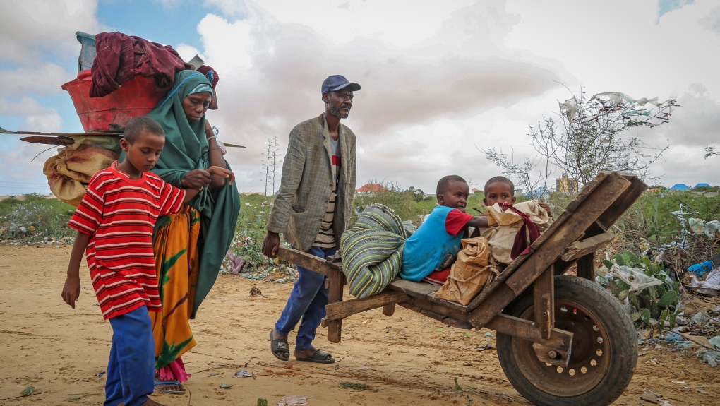 A local resident uses a wheelbarrow to transport the young children of a woman who fled drought-stricken areas as she arrives at a makeshift camp for the displaced on the outskirts of Mogadishu, Somalia Thursday, June 30, 2022. (AP Photo/Farah Abdi Warsameh)
