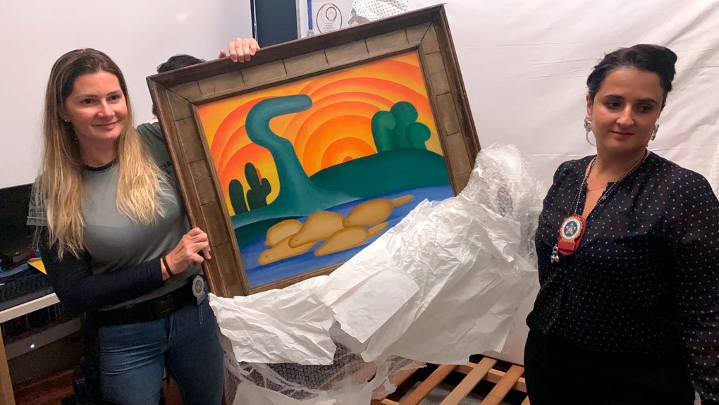 In this photo provided by the Rio de Janeiro Civil Police, officers show artist Tarsila do Amaral's painting titled 'Sol Poente' after it was seized during a police operation in Rio de Janeiro, Brazil, Wednesday, Aug. 10, 2022. (Rio de Janeiro Civil Police via AP)