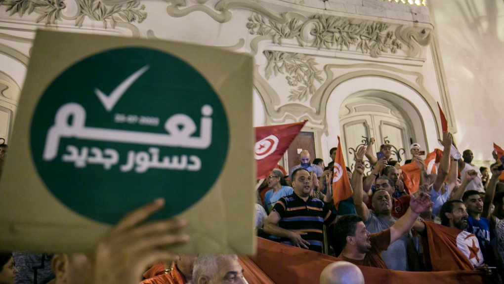A Tunisian holds a sign reading 'Yes to the new constitution' as others celebrate exit polls that indicate a vote in favor of the new constitution, in Tunis, July 25, 2022. (AP Photo/Riadh Dridi, file)