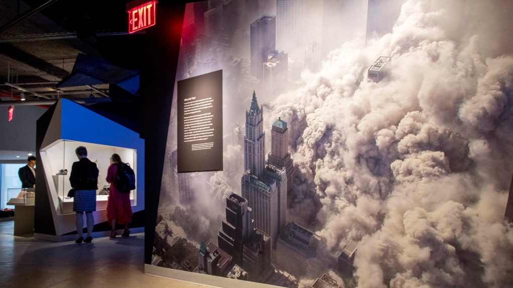 In this Thursday, June 8, 2017, photo, a giant photograph showing the cloud of debris that covered lower Manhattan after the collapse of one of the World Trade Center towers is on display next to visitors to a preview at the 9/11 Tribute Museum in New York. (AP Photo/Mary Altaffer)