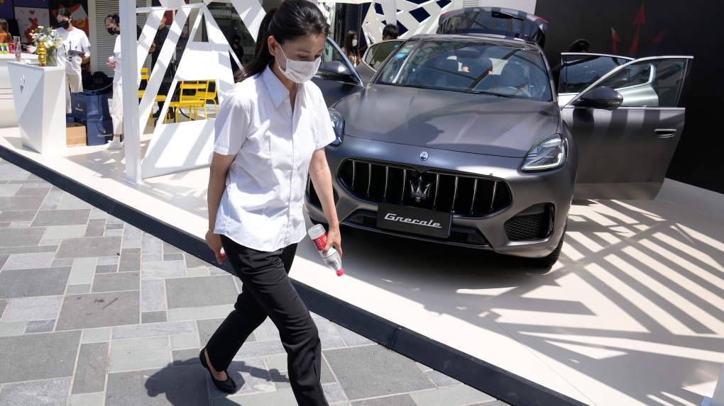 A worker wearing a mask past by a luxury car displayed at a mall, Wednesday, July 13, 2022, in Beijing.  (AP Photo/Ng Han Guan)