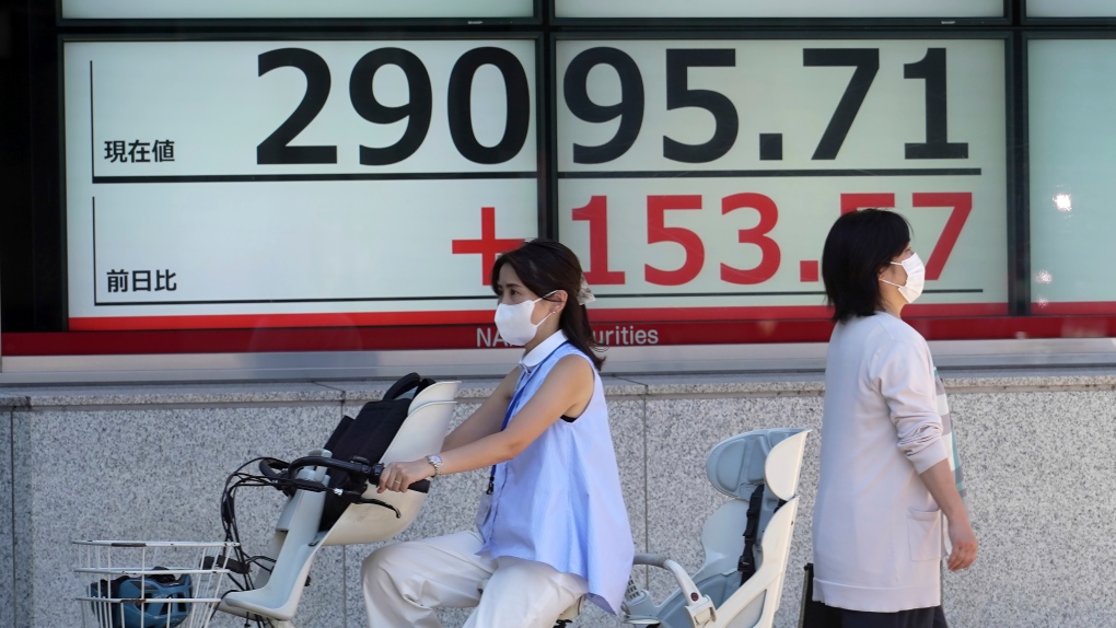 People wearing protective masks wait for traffic light changing in front of an electronic stock board showing Japan's Nikkei 225 index at a securities firm Friday, Aug. 19, 2022, in Tokyo. (AP Photo/Eugene Hoshiko)