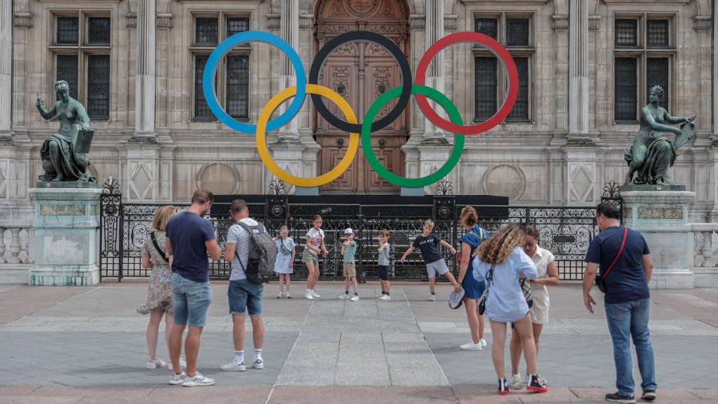 People gather at the Olympic rings at the City Hall in Paris, Monday, July 25, 2022. (AP Photo/Lewis Joly)