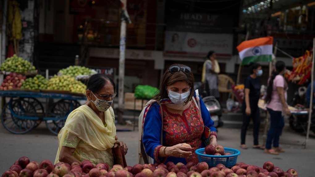 Women wearing masks buy apples from a roadside vendor in New Delhi, India, Thursday, Aug. 11, 2022.  (AP Photo/Altaf Qadri)