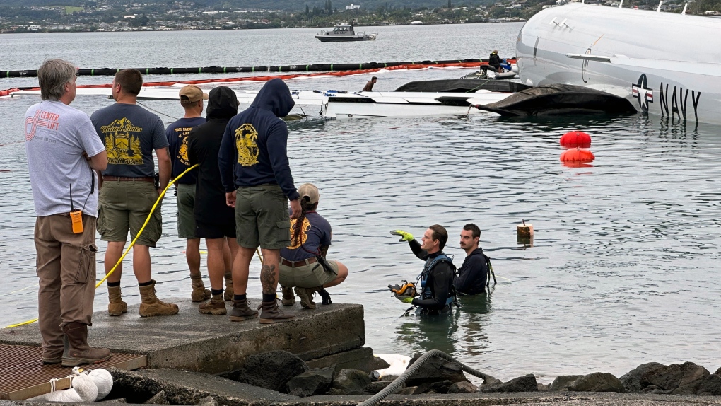 Contractors place inflatable bags under a U.S. Navy P-8A in Kaneohe Bay, Hawaii, Friday, Dec. 1, 2023, so they can float the aircraft over the water and onto land. The Navy plans to use inflatable cylinders to lift the jet off a coral reef and then roll it over to a runway to remove the plane from the ocean where it crashed the week before. (AP Photo/Audrey McAvoy)