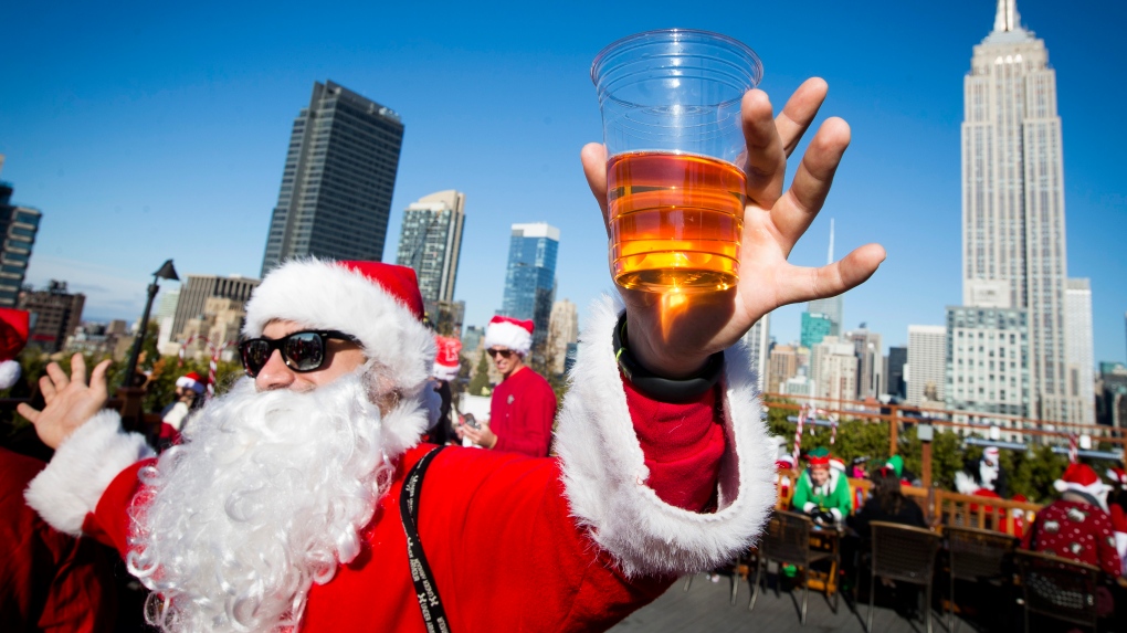 FILE - A man dressed as Santa Claus holds a beer as he and others participate in SantaCon on a rooftop bar Saturday, Dec. 13, 2014, in New York. Thousands of people dressed as jolly Old St. Nick have descended on New York City for the annual SantaCon charity pub crawl. The booze-fueled stroll through Manhattan kicked off Saturday morning, Dec. 9, 2023, in bars in midtown. (AP Photo/John Minchillo, File)