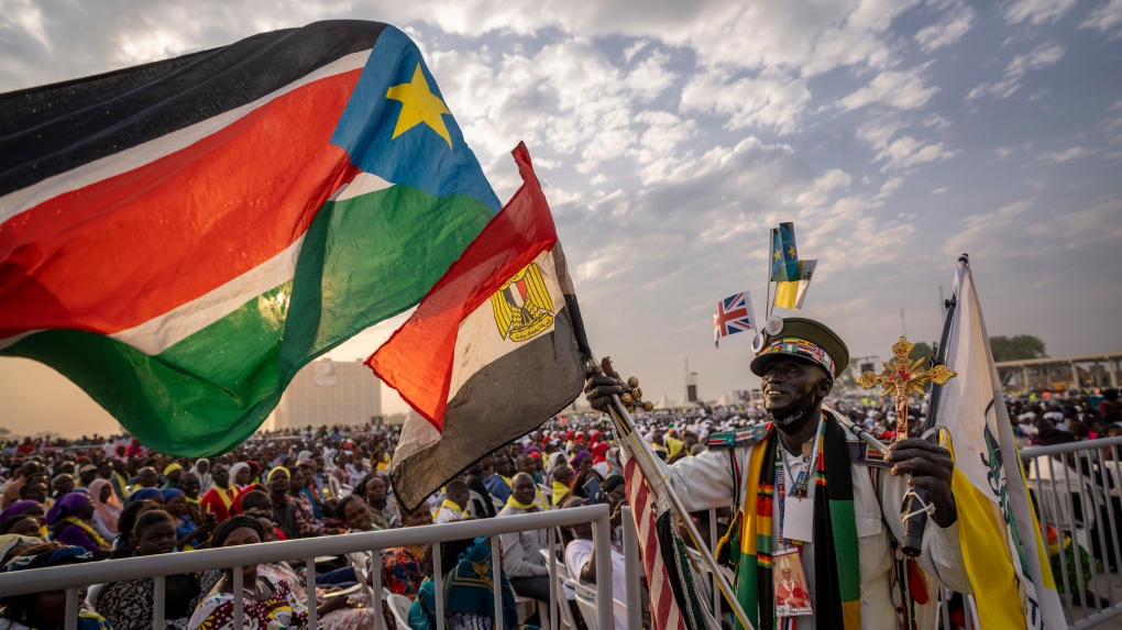 A man holds flags next to the audience as they await the arrival of Pope Francis for a Holy Mass at the John Garang Mausoleum in Juba, South Sudan on Feb. 5, 2023. Pope Francis is in South Sudan on the final day of a six-day trip that started in Congo, hoping to bring comfort and encouragement to two countries that have been riven by poverty, conflicts and what he calls a "colonialist mentality" that has exploited Africa for centuries. (AP Photo/Ben Curtis)