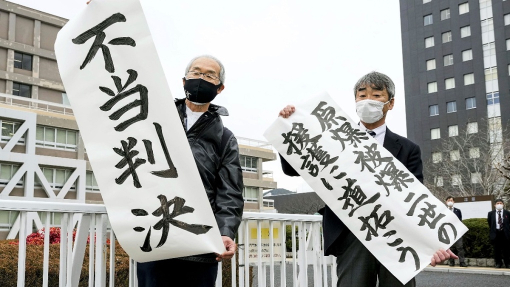 Plaintiff Katsuhiro Hirano, right, and an unidentified lawyer for the plaintiffs display signs after a judgement at Hiroshima District Court in Hiroshima, western Japan, Feb. 7, 2023. The banners read, "Pave the way to back up Second-Generation Atomic Bomb Survivors," right, and, "Unfair judgement." (Kyodo News via AP)