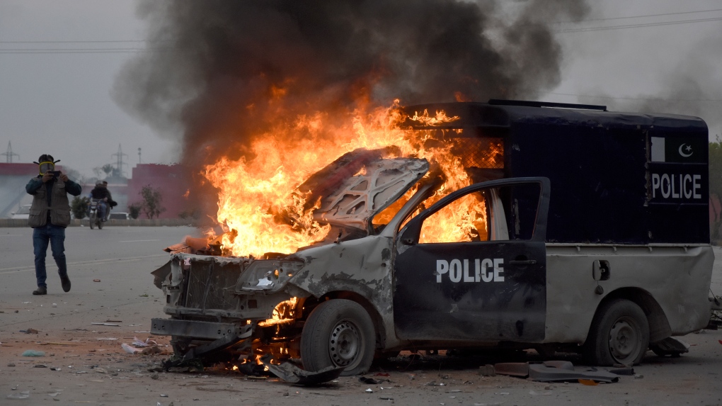A man films with his mobile phone to a burning police vehicle following the clashes between police and the supporters of former Prime Minister Imran Khan, at outside the a court, in Islamabad, Pakistan, March 18, 2023. Pakistani police stormed former Prime Minister Khan's residence in the eastern city of Lahore on Saturday and arrested 61 people amid tear gas and clashes between Khan's supporters and police, officials said. (AP Photo/W.K. Yousafzai)