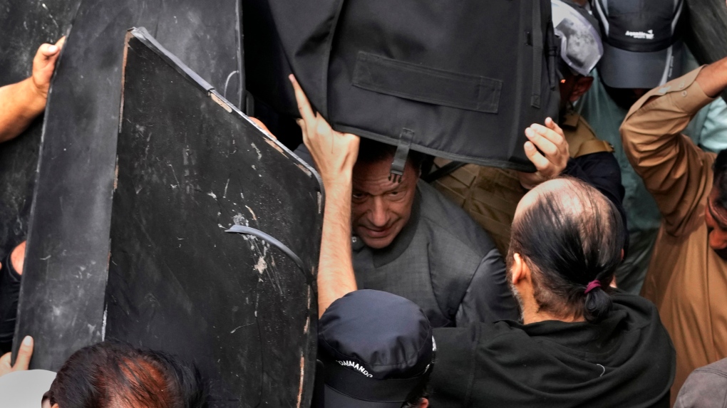 Security personnel hold bulletproof shields to secure former Prime Minister Imran Khan, centre, after appearing in a court, in Lahore, Pakistan, Tuesday, March 21, 2023.  (AP Photo/K.M. Chaudary)