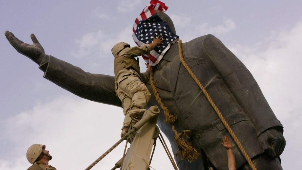 In this April 9, 2003, file photo, an Iraqi man, bottom right, watches Cpl. Edward Chin of the 3rd Battalion, 4th Marines Regiment, cover the face of a statue of Saddam Hussein with an American flag before toppling the statue in downtown Baghdad, Iraq. (AP Photo/Jerome Delay, File)