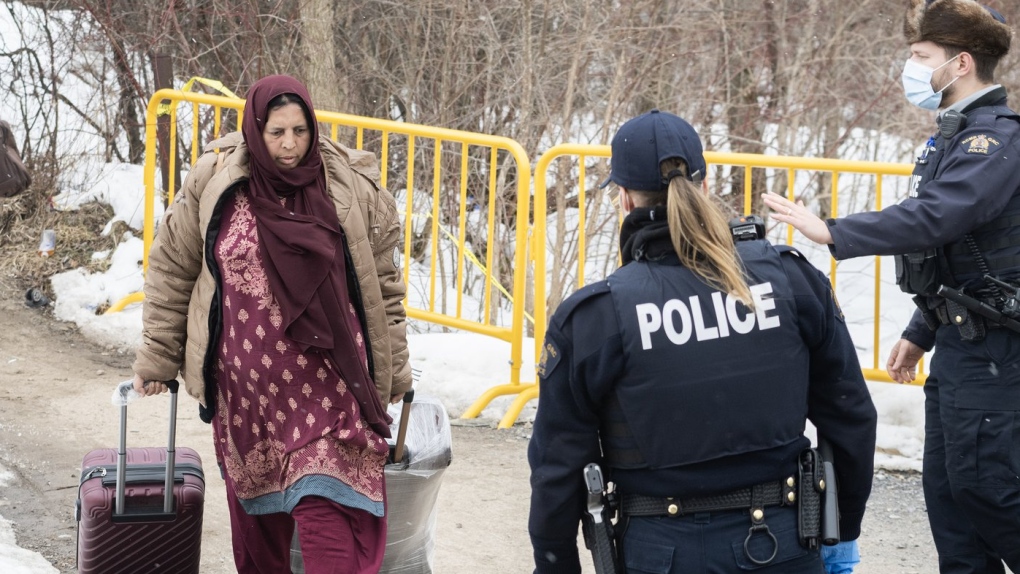 RCMP officers approach a woman entering Canada via Roxham road on the Canada/US border in Hemmingford, Que., Saturday, March 25, 2023. (THE CANADIAN PRESS/Graham Hughes)