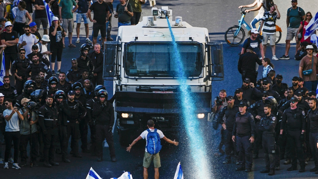 A person stands in front of an Israeli police water cannon being used to disperse demonstrators blocking a road during a protest against plans by Prime Minister Benjamin Netanyahu's government to overhaul the judicial system, in Jerusalem, Monday, July 24, 2023. Israeli lawmakers on Monday approved a key portion of Prime Minister Benjamin Netanyahu's divisive plan to reshape the country's justice system despite massive protests that have exposed unprecedented fissures in Israeli society. (AP Photo/Ariel Schalit)