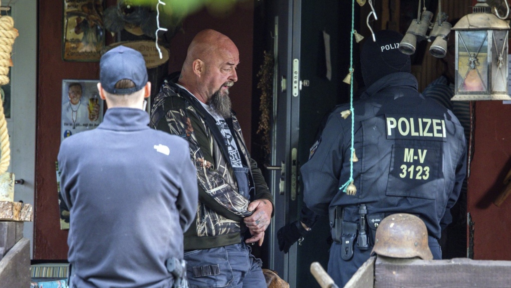 Sven Krueger, left, a right-wing extremist known throughout Germany, stands between police officers during a search operation on his property in Jamel, Germany, Tuesday, Sept. 19, 2023. (Jens Buettner/dpa via AP)