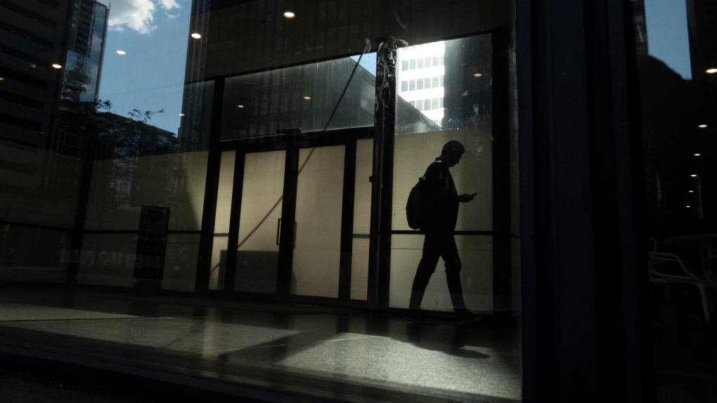 A person walks though a downtown Toronto office building with other buildings reflected in a window in this June 11, 2019 photo. THE CANADIAN PRESS/Graeme Roy