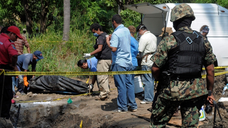 A Mexican Navy soldier watches as forensic workers remove a body which was buried at a field in the town of Tuncingo, southern Mexico, Wednesday Nov. 3, 2010. (AP / Bernandino Hernandez)