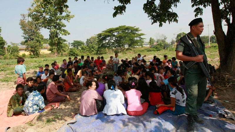 Myanmar citizens, who fled the fighting between Myanmar soldiers and Karen fighters, are guarded by a Thai border police officer as they gather under the tree in a field in Mae Sot town, Thailand Monday, Nov. 8, 2010. (AP / Apichart Weerawong)