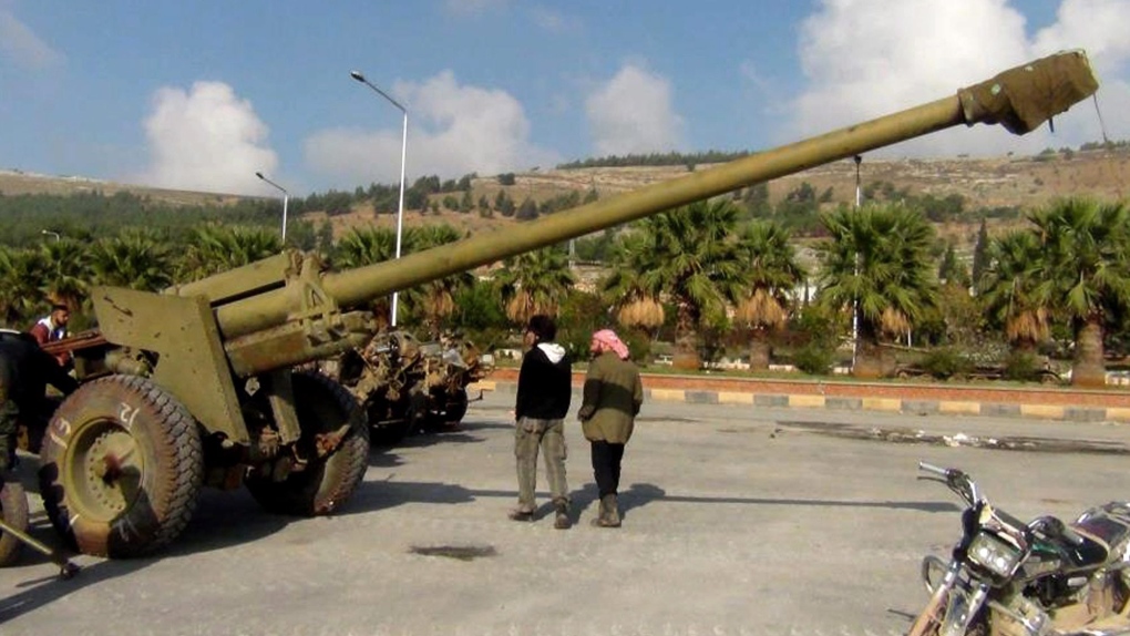 Syrian rebels walk next to a cannon 