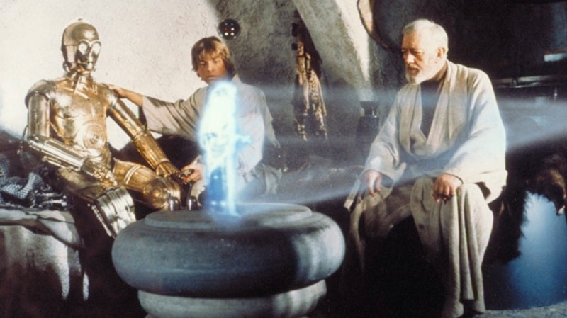 From left, Anthony Daniels portraying C-3PO, Mark Hamill portraying Luke Skywalker and Alec Guinness portraying Ben Obi-Wan Kenobi look at a hologram of Princess Leia, portrayed by Carrie Fisher in a scene from the original 1977 'Star Wars' film.