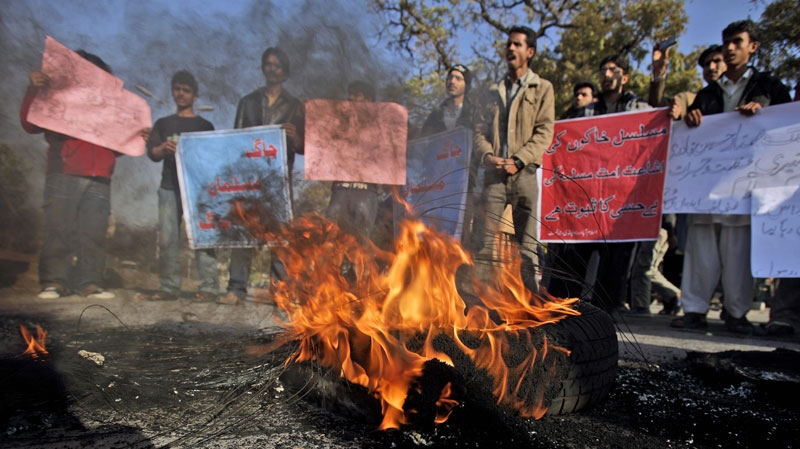 Pakistanis stand next to burning tyres holding banners and chanting slogans during a protest in support of Mumtaz Qadri, alleged killer of Punjab governor Salman Taseer, in Islamabad, Pakistan, Monday, Jan. 10, 2011. (AP Photo/Muhammed Muheisen)