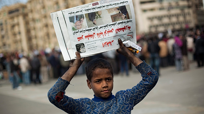 A boy sells newspapers and cigarettes as anti-government protesters, background, gather in Tahrir Square in Cairo, Sunday, Jan. 30, 2011. (AP / Emilio Morenatti)