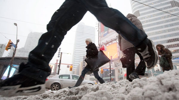 A woman is framed by a man leaping over a snowbank as pedestrians make their way through the snow at Yonge St. and Dundas Square in downtown Toronto Wednesday, Feb. 2, 2011. (Darren Calabrese / THE CANADIAN PRESS)
