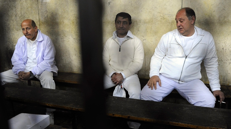 Three former Egyptian officials ex-Housing Minister Ahmed Maghrabi, left, former Tourism Minister Zuheir Garana, right and steel tycoon and prominent ruling party leader Ahmed Ezz, centre, wear white prison uniforms and sit in a metal cage as they appeared in a Cairo Criminal Court in Cairo, Egypt, Thursday, Feb. 24, 2011. (AP)