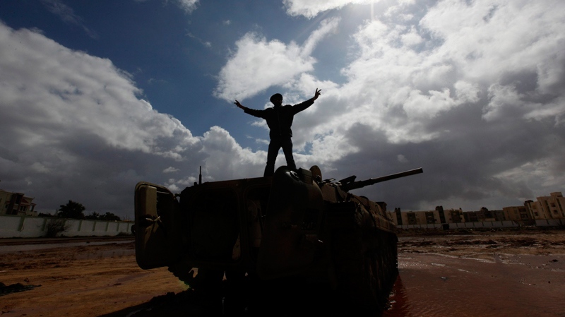 A Libyan man stands over a destroyed tank as he flashes V signet Al-Katiba military base after it fell to anti-Libyan Leader Moammar Gadhafi in Benghazi, Libya, on Thursday Feb. 24, 2011. (AP / Hussein Malla)