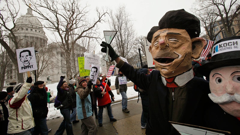 Ted McManus, second from right, wears a mask of Wisconsin Gov. Scott Walker, beside Laurie Rossbach, right, wearing a Mr. Monopoly mask, while people demonstrate over the governor's proposal to strip most public employees of their collective-bargaining rights in front of the state Capitol in Madison, Wis., Saturday, Feb. 26, 2011. (AP Photo/Andy Manis)