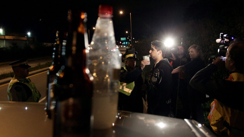 Open bottles of alcohol found in a motorist's car sit on the vehicle as RCMP Cnst. Kim True conducts a breathalyzer test on the driver during a roadside check in Surrey, B.C., just before midnight on Friday, Sept. 24, 2010. (Darryl Dyck / THE CANADIAN PRESS)