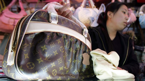 A shop assistant displays a fake Louis Vuitton bag at a store in Beijing Wednesday April 19, 2006. (AP / Greg Baker)