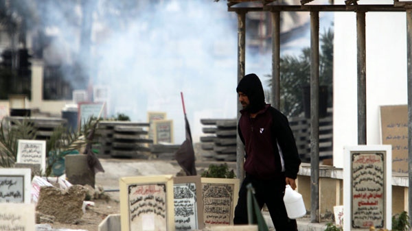 An anti-government protester carrying water to throw on tear gas canisters fired by riot police, moves through a cemetery Thursday, March 17, 2011, as gas billows behind him in the Shiite Muslim village of Jidhafs, Bahrain, on the outskirts of the capital of Manama. Security forces are moving through Shiite villages, cracking down and making arrests. 