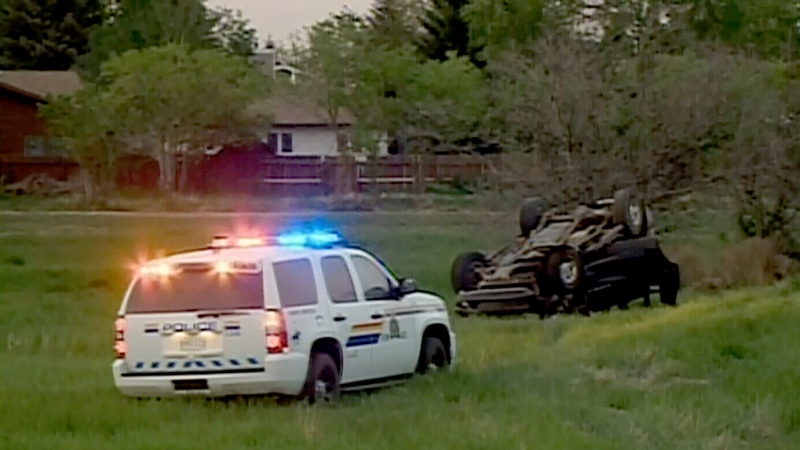 A police vehicle sits in the grass near an overturned car in Saskatoon, on Saturday, June 1, 2013. (CTV Winnipeg)