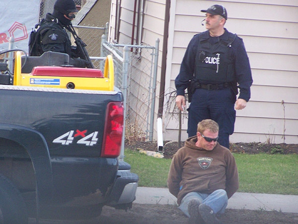 A suspect sits handcuffed on the curb as police keep watch.