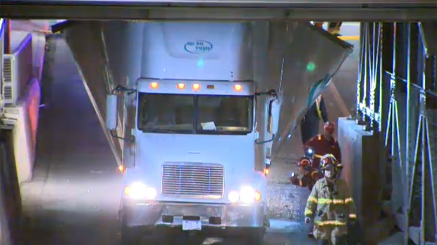 Semi truck and trailer wedged under bridge