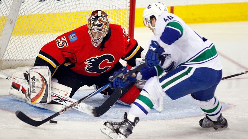 Vancouver Canucks' Maxim Lapierre, right, tries to get the puck past Calgary Flames goalie Henrik Karlsson, from Sweden, during first period NHL hockey action in Calgary, Alta., Saturday, April 9, 2011. (Jeff McIntosh / THE CANADIAN PRESS)