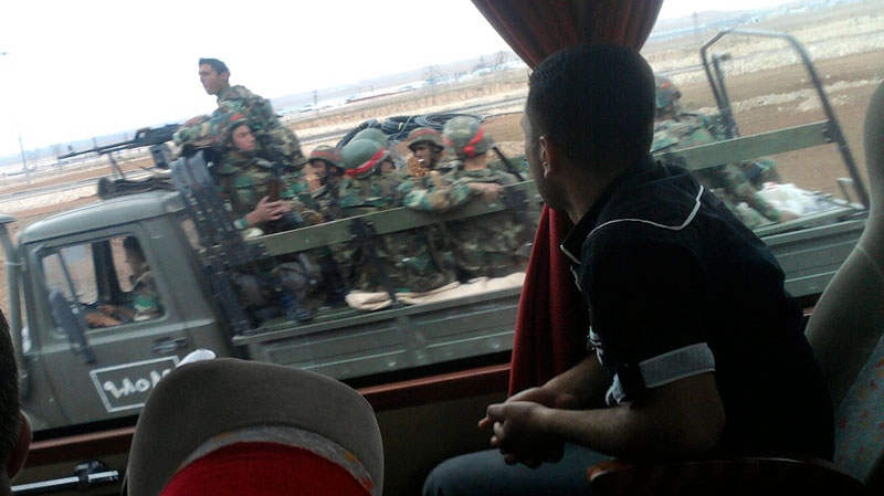 In this image made on a mobile phone, a Syrian man sits inside a bus as he looks through the window at  a military truck carrying Syrian soldiers, in the outskirts of the central city of Homs, Syria, on Thursday April 21, 2011. (AP Photo)