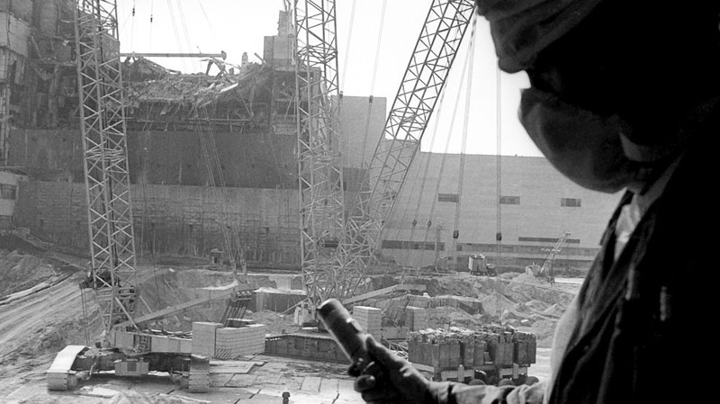 A Chernobyl nuclear power plant worker holding a dosimeter to measure radiation level is seen against the background of a sarcophagus under construction over the 4th destroyed reactor on this file photo taken in 1986. (AP Photo/Volodymyr Repik)
