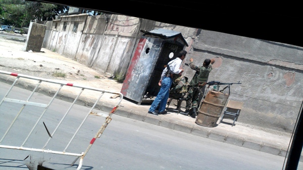 In this image made on a mobile phone from the window of a car, two Syrian soldiers and an armed man in civilian clothes stand at a checkpoint in Damascus, Syria, Sunday, May 1, 2011. (AP Photo)