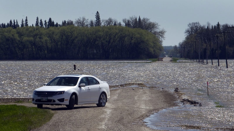 A car turns around as the waters from the Assiniboine River breach flood across a road Tuesday, May 17, 2011 near Newton, Manitoba. (THE CANADIAN PRESS/Ryan Remiorz)